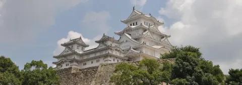 Burg Himeji mit weißer Außenfassade auf einer Mauer mit grünen Bäumen davor
