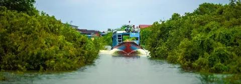 Boot mit Personen fährt über das Wasser eines Flusses mit grüner Vegetation am Ufer