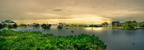 Tonle Sap See mit Häusern und grünem Ufer bei bewölkter Sonnenuntergangsstimmung.