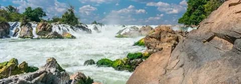 Breiter Wasserfall Khon Phapheng in Laos mit starker Strömung zwischen Felsen und grünen Pflanzen.