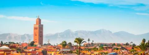 Marakesch mit markantem Turm im Vordergrund und Gebirgskette des Atlasgebirge im Hintergrund.