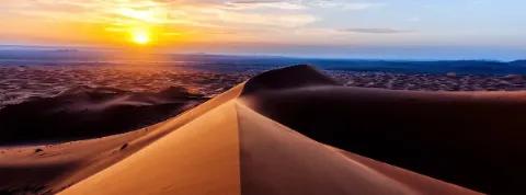 Sonnenuntergang über großen Sanddüne in der Erg Chebbi-Wüste mit wellenförmigen Strukturen in Wüstenlandschaft.