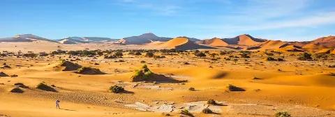 Die Dünenlandschaft der Namib-Wüste mit einer Frau, die mit einer Kamera eine Landschaft fotografiert.