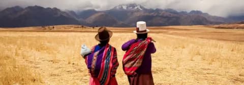 Zwei Frauen in traditioneller Kleidung stehen auf einem Feld im Heiligen Tal in den Anden unter bewölktem Himmel.