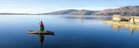 Eine Frau in traditioneller Kleidung paddelt in einem Holzboot auf dem ruhigen Titicacasee.