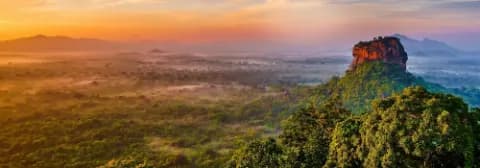 Panoramablick auf den Sigiriya-Felsen von Bergen und üppigem Grün umgeben bei Sonnenaufgang.