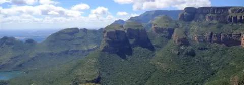 Ausblick über de grünen Berghänge des Blyde-River-Canyon unter leicht bewölktem Himmel