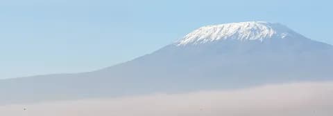 Der schneebedeckte Berg Kilimandscharo erhebt sich über einem Wolkenmeer unter strahlend blauem Himmel.