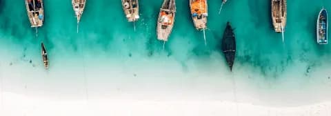 Luftaufnahme mit hölzernen Fischerbooten im türkisfarbenen Wasser nahe eines weißen Sandstrandes in Sansibar.