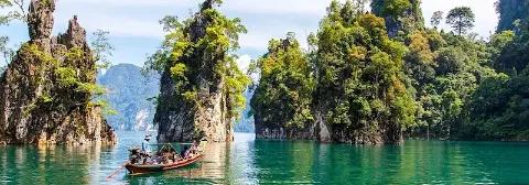 Mann auf einem Boot fährt über den smaragdgrünen Cheow Lan See im Khao Sok Nationalpark, umgeben von Kalksteinfelsen.