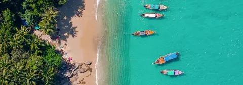 Luftaufnahme von vier Langbooten, die auf türkisfarbenem Meer nahe dem von Palmen gesäumten Sandstrandes treiben.