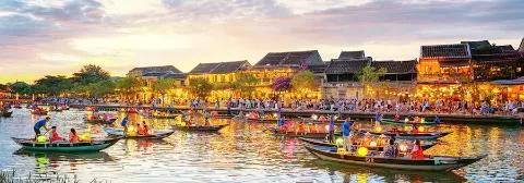 Hoi An am Abend mit beleuchteten Häusern am Ufer und Booten mit Lampions auf dem Fluss.