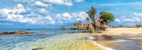 Weißer Sandstrand auf Phu Quoc mit klarem Wasser, Felsen und einem Haus unter blauem Himmel mit Wolken.