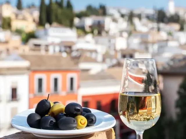 Ein Teller mit Oliven und ein Glas Weißwein, mit einer malerischen Stadt im Hintergrund.
