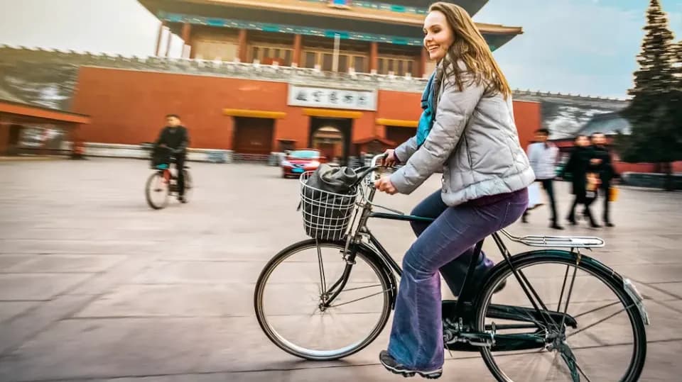 Touristin auf dem Fahrrad fährt an der Verbotenen Stadt in Peking vorbei mit Menschen im Hintergrund.