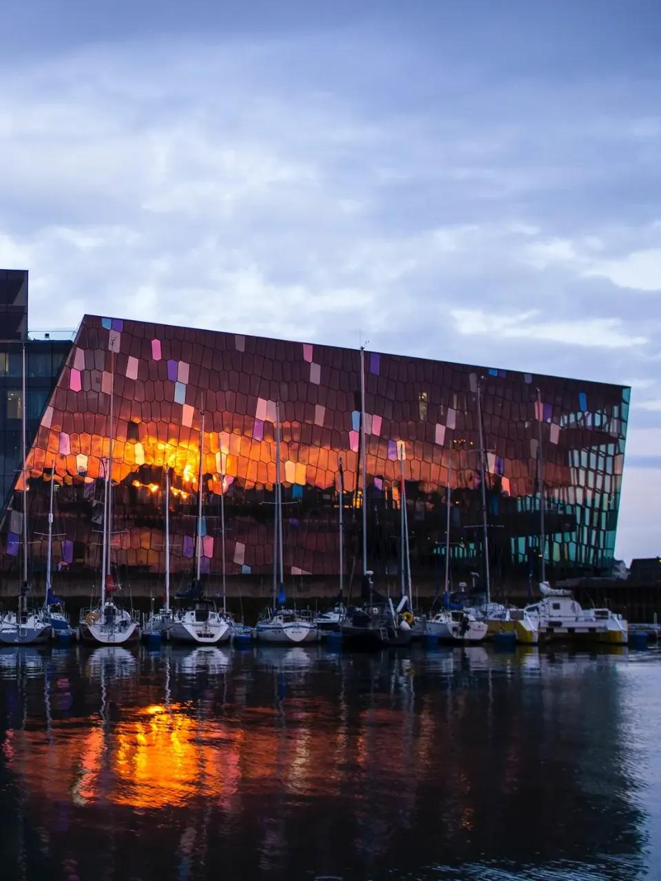 Modernes Gebäude mit reflektierenden Fenstern am Hafen bei Sonnenuntergang.