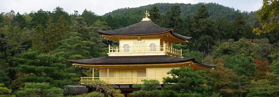 Goldener Pavillion in Kyoto umrundet von grünen Bäumen unter bewölktem Himmel