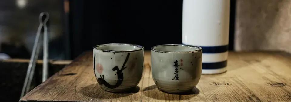 Zwei typisch japanische Gläser mit einer Flasche Sake auf einem Holzbrett