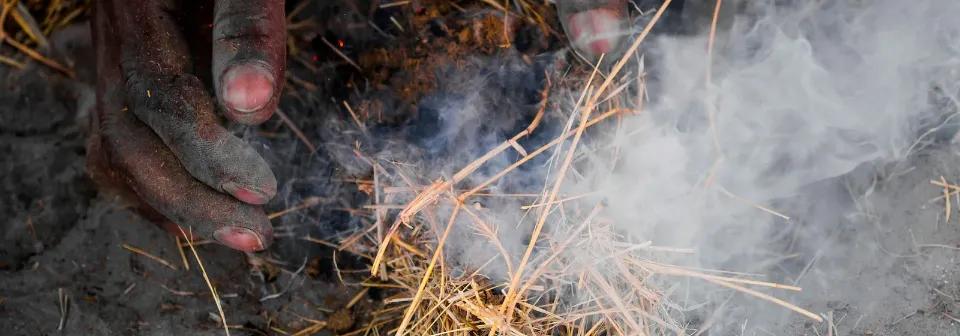 Afrikanische Hand versucht ein Feuer zu machen per Hand und das Stroh qualmt