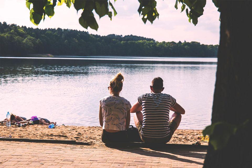 Zwei Personen sitzen am Ufer mit Blick auf das Wasser.
