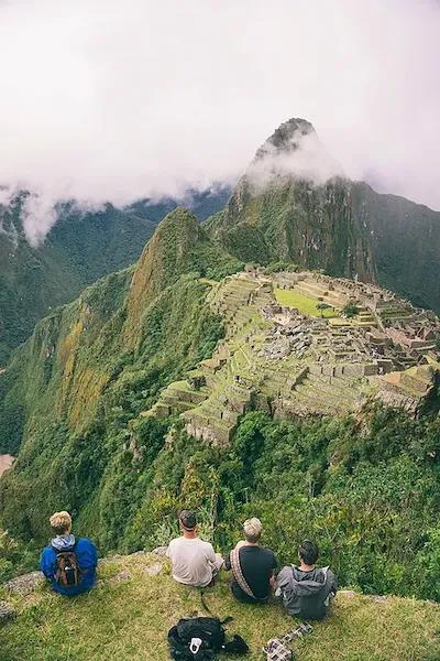 Drei Personen sitzen auf grüner Wiese und schauen auf die Inka-Stätte Machu Picchu