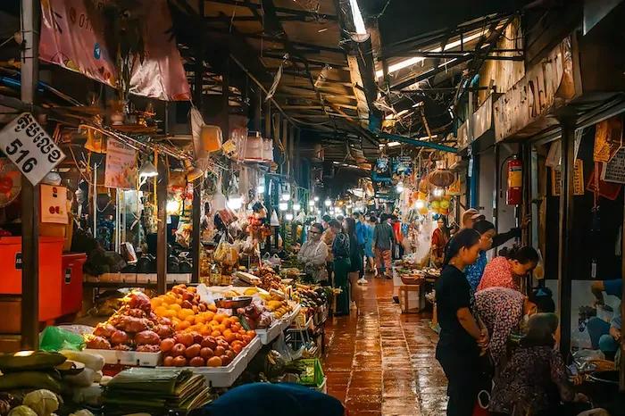 Menschen tummeln sich an verschiedenen Marktständen mit Früchten in Phnom Penh bei Nacht.