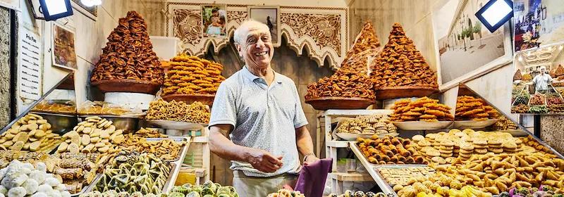 Ein lächelnder Konditoreibesitzers, der in seinem Geschäft in den Souks von Marrakesch steht.