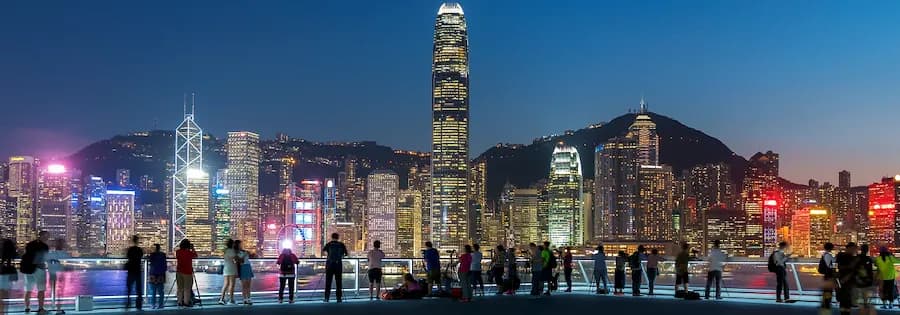 Menschen stehen vor der leuchtenden Skyline von Hongkong am Hafen bei Abenddämmerung.