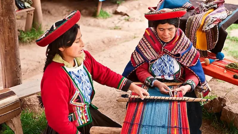 Zwei Frauen in traditioneller Kleidung weben farbenfrohe Textilien in Peru mit traditioneller Handwerkskunst.