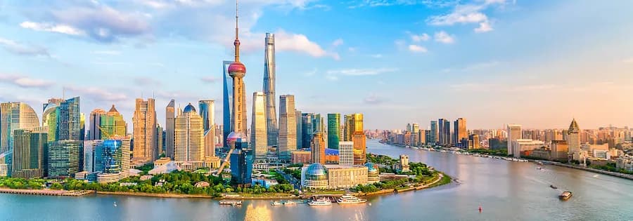 Panoramaaufnahme der Skyline von Shanghai mit mehreren Hochhäusern und einem Fluss im Vordergrund.