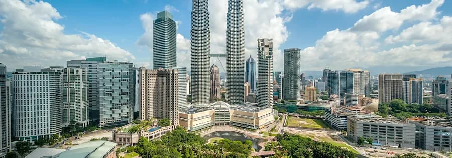 Blick auf die Skyline von Kuala Lumpur mit den Petronas Twin Towers unter leicht bewölktem Himmel.
