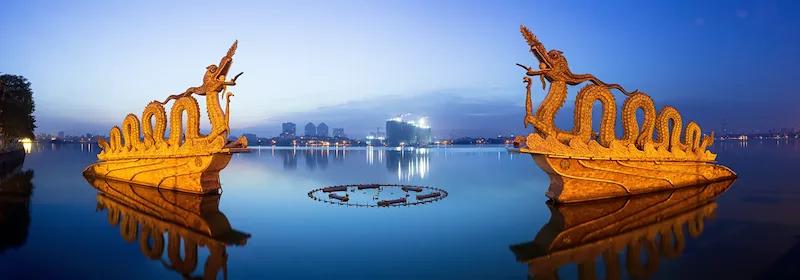 Zwei Drachenstatuen auf dem Westsee in Hanoi werden angeleuchtet in einer Abendstimmung.