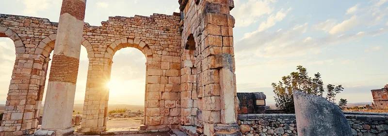 Blick auf einen steinernen Torbogen in den Ruinen der antiken Stadt Volubilis bei Sonnenuntergang in Marokko.
