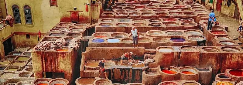 Mehrere Menschen arbeiten zwischen runden Gerbgruben in einer traditionellen Gerberei in Fes mit gefärbten Flüssigkeiten.