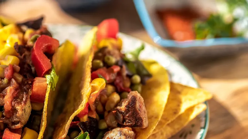 Auf einem Teller liegen zwei mexikanische Tacos, gefüllt mit Mais, Fleisch und Paprika.