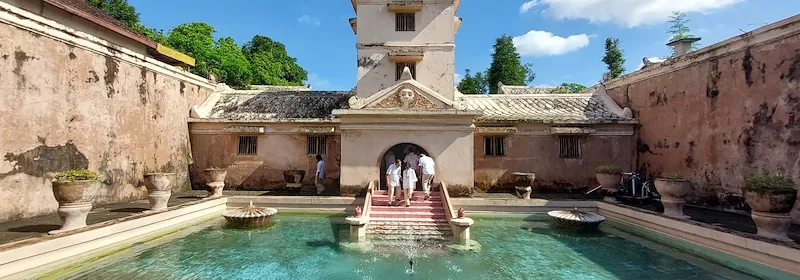 Hof vom Wasserschloss Tamansari mit klarem Wasserbecken und Brunnen unter blauem Himmel.