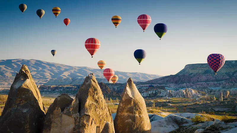 Mehrere Heißluftballons schweben über der Landschaft von Kappadokien mit markanten Felsformationen.