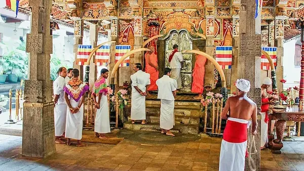 Mehrere Menschen in weißen Gewändern stehen und knien in einem reich verzierten Tempel vor einer Statue.
