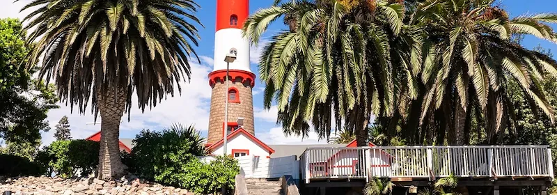 Ein Leuchtturm in Swakopmund umgeben von Palmen und einer Küstenlandschaft mit Promenade.