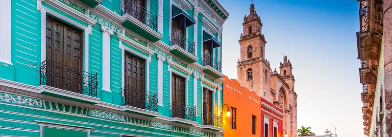 Bunte Hausfassaden und eine Kathedrale in Mérida mit blauem Himmel