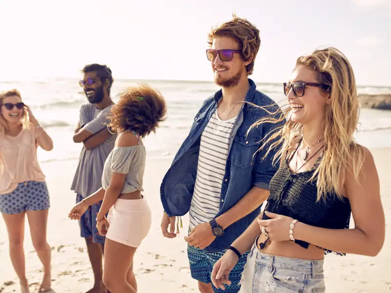 Eine Gruppe junger Menschen lacht zusammen am Strand.