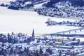 Winterliche Ansicht bei Ihrer Reise nach Lillehammer in Norwegen - mit seinen verschneiten Dächern, Kirche und einer Brücke über einen teilweise zugefrorenen Fluss.