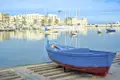 Blaues Fischerboot im Hafen von Bari, weitere Boote und Gebäude im Hintergrund.