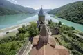 Die historische Wehrkirche Ananuri in Georgien am Ufer des türkisgrünen Schinwali-Stausees vor Kaukasus-Bergkulisse.