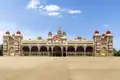 Außenansicht des Mysore-Palasts mit seinen vielen Kuppeln und Bögen vor blauem Himmel.