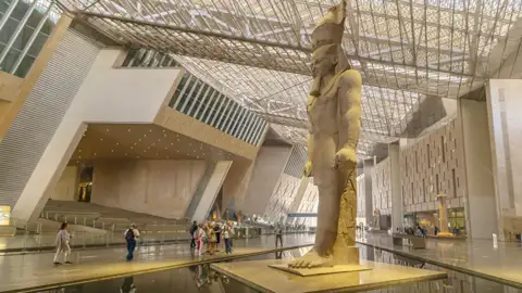 Reisende bestaunen die riesige Pharaonenstatue in der modernen, lichtdurchfluteten Halle des Grand Egyptian Museum in Kairo.