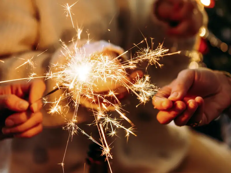 Nahaufnahme von Händen, die auf einer Gruppenreise für junge Leute in Dublin eine leuchtende Wunderkerze zur Silvesterfeier halten.