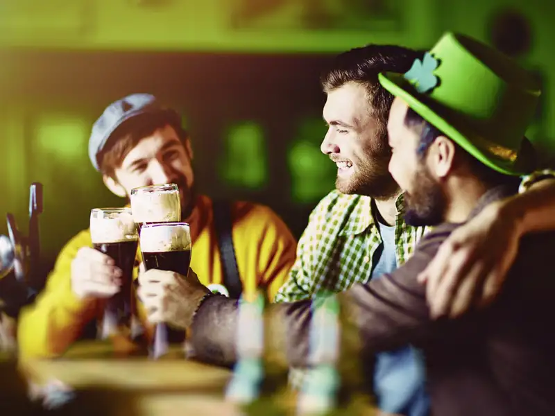 Junge Freunde stoßen auf einer Gruppenreise für junge Leute in einem Pub in Dublin fröhlich mit dunklem Bier an.