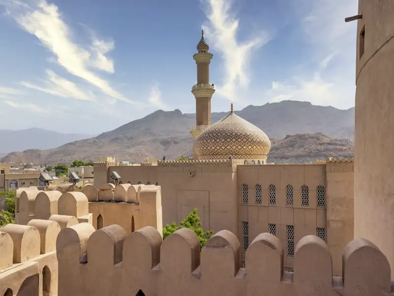 Auf Ihrer Reise durch den Oman sehen Sie den Turm des Forts, das höchste Gebäude in Nizwa. Der Blick schweift über die Neu- und die Altstadt, die Gärten und Lehmhäuser bis hinüber zu den Bergen.