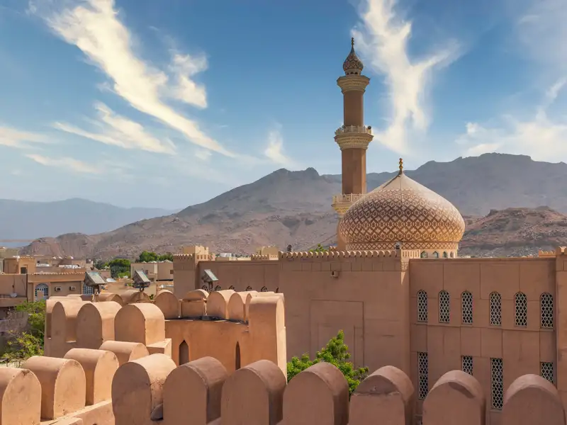 Auf Ihrer individuellen Rundreise durch den Oman sehen Sie in Nizwa den Turm des Forts, das höchste Gebäude in Nizwa: Der Blick schweift über die Neu- und die Altstadt, die Gärten und Lehmhäuser bis hinüber zu den Bergen.